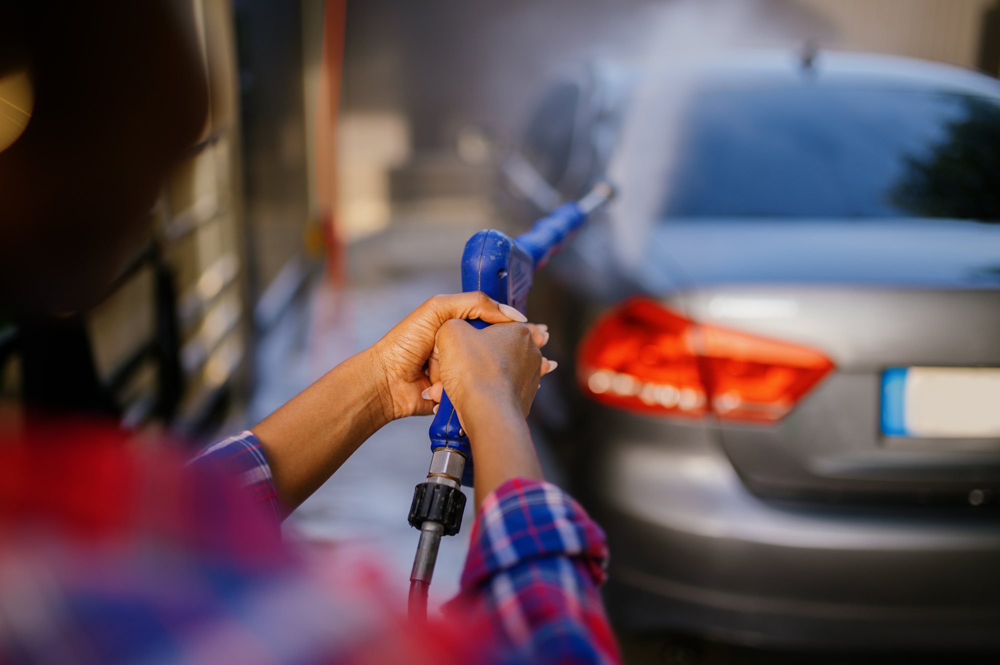 Woman using high pressure water gun, car wash